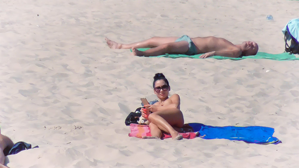 Zwei Frauen sonnen sich oben ohne auf Handtüchern im Sand