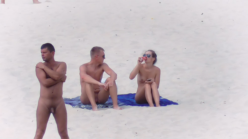 Twee nudisten zittend op een blauwe handdoek aan de oever