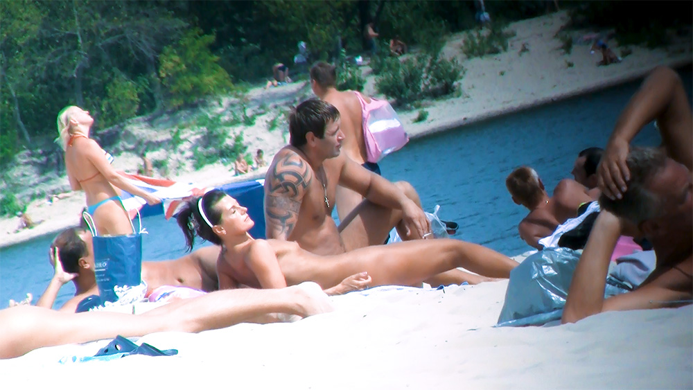 Two Nudists Resting on the Sand by the Shore