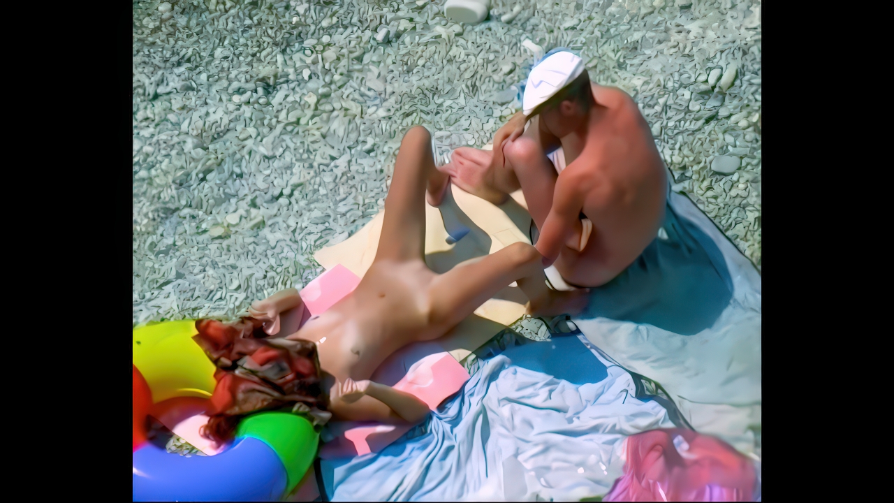 Nudist woman lounging on yellow towels at a sunny pebble beach