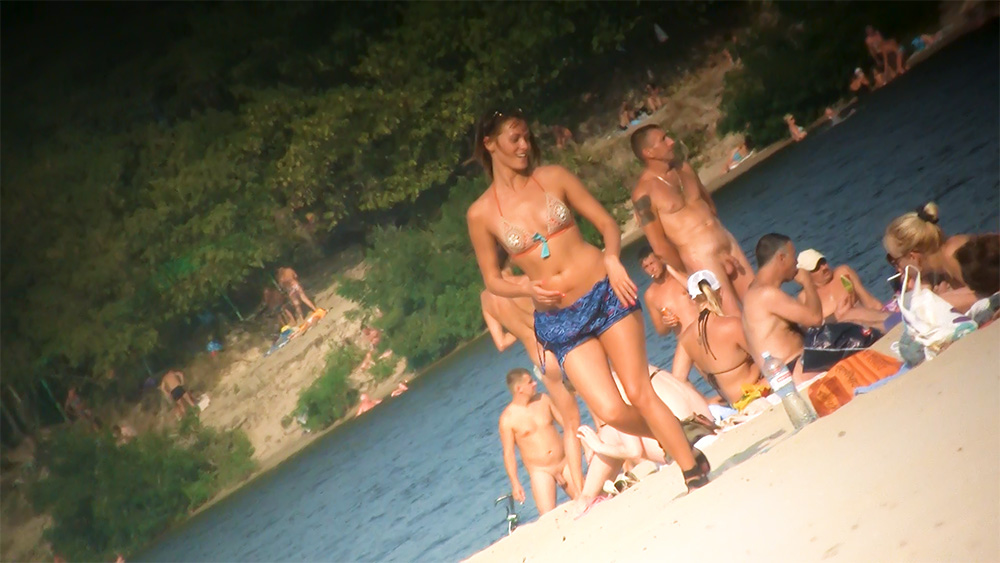 Six Naturists Standing and Sitting on a Sandy Riverbank