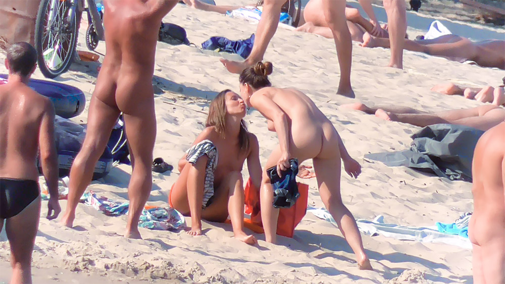 Strandmoment zwischen zwei Naturistinnen mit oranger Tasche