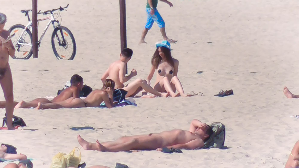 Tři dospělí na topless pláži poblíž dřevěného kůlu