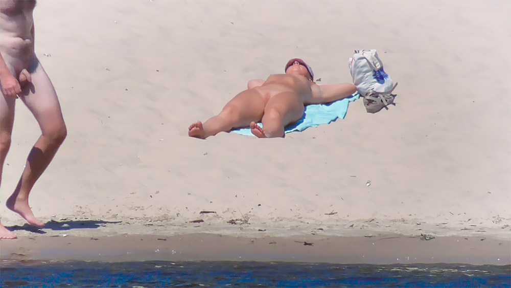 Opalování na břiše na modrém ručníku na nudistické pláži