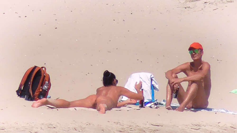Žena na nudistické pláži vedle oranžového batohu