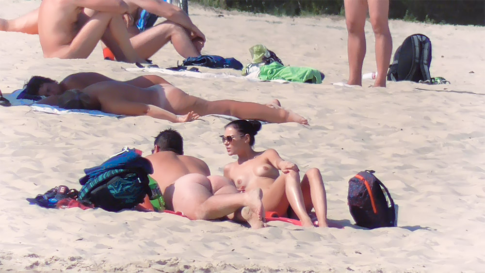 Three Nudists Sitting Together on Sunlit Sand