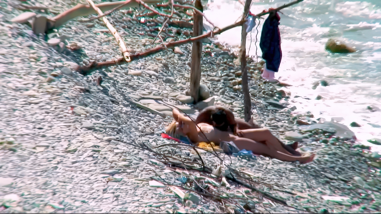Voorspel op de kiezelkust, naturisten op een handdoek bij het zonovergoten water