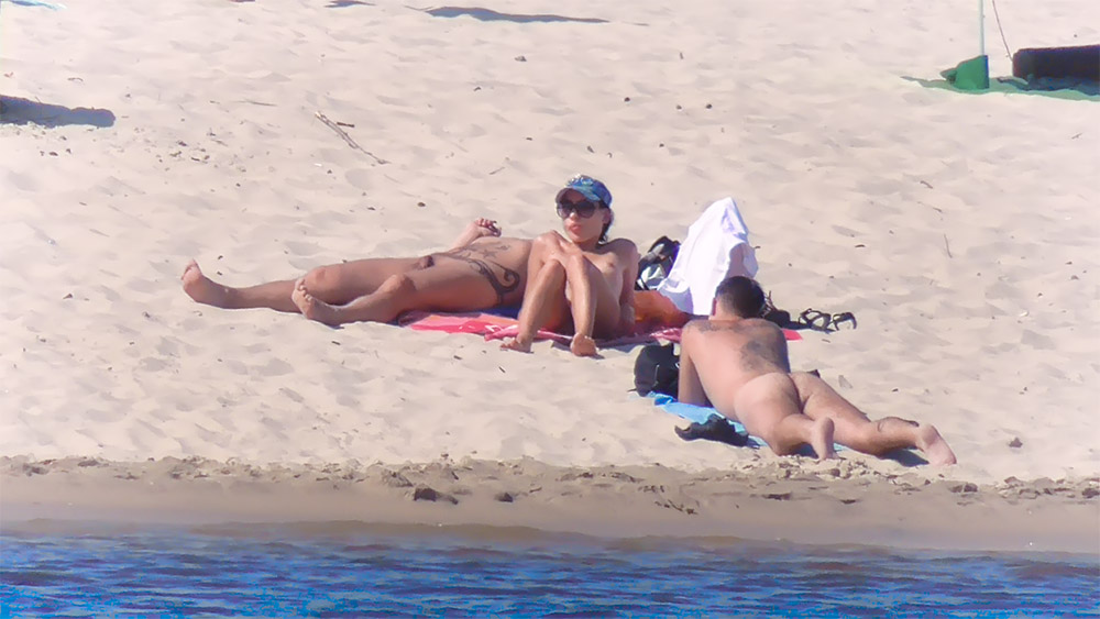 Tři naturisté odpočívající na písečné pláži