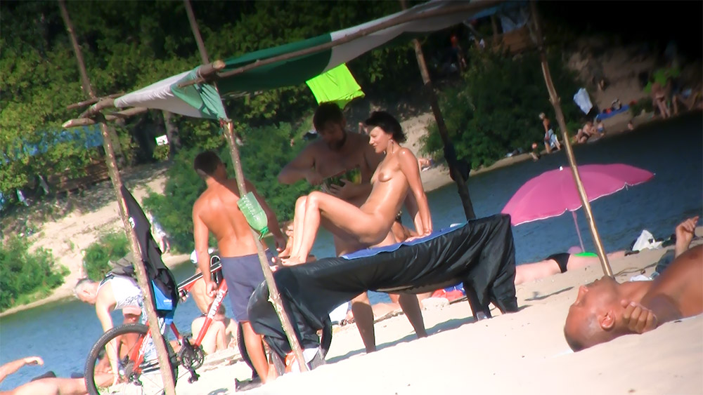 Quatro Nudistas Reunidos à Volta de uma Espreguiçadeira à Sombra