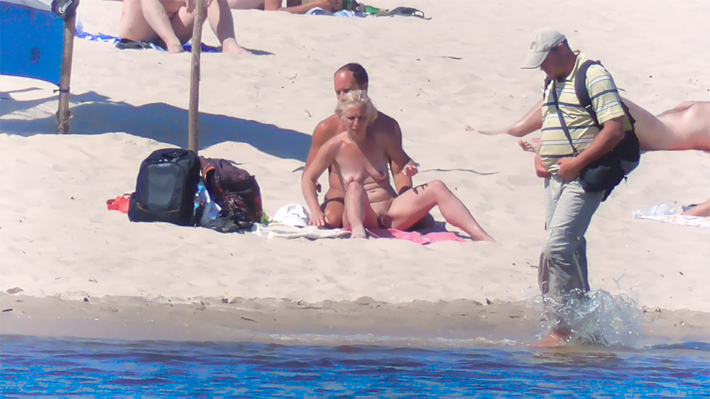 Three Nudists Gathered Near an Orange Windbreak