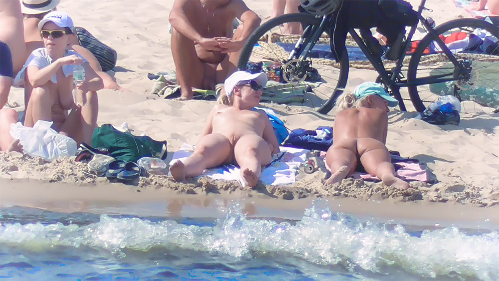 Two Nudists Lounging on Towels Near the Shoreline