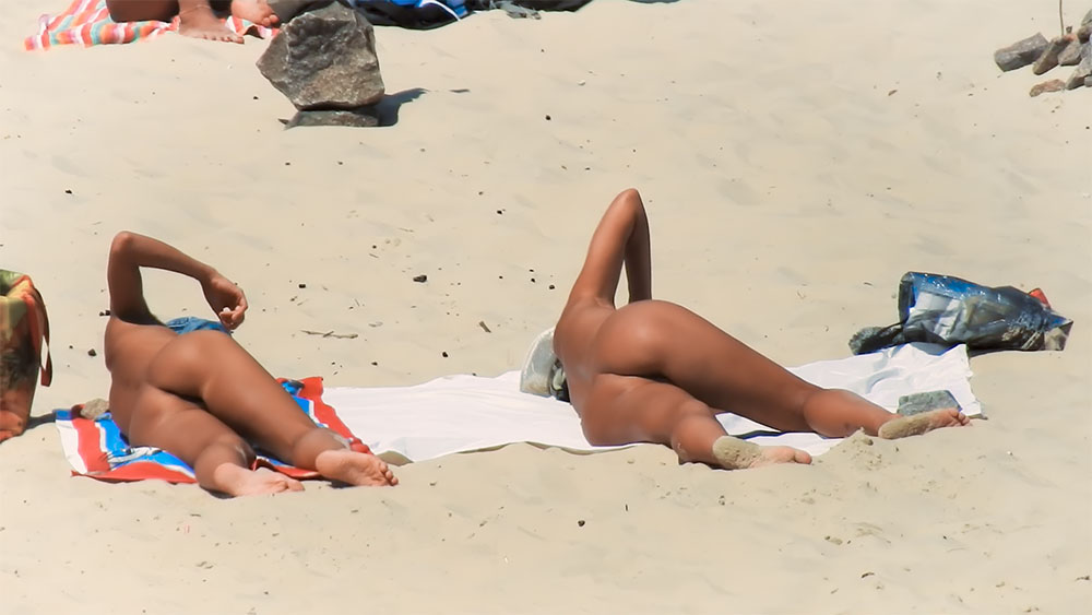 Ležení na břiše se zvednutým kolenem na ručníku na nudistické pláži