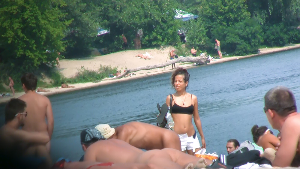 Four Naturists Resting on a Sandy River Shore