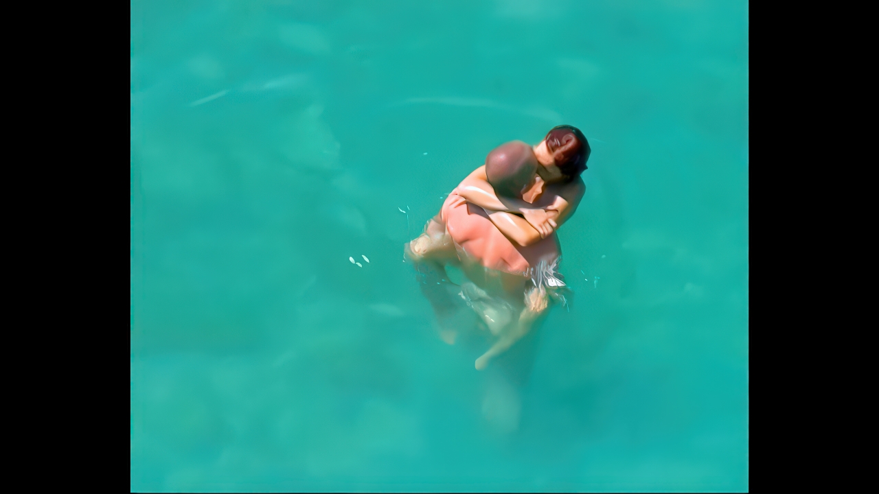 Zwei Naturisten umarmen sich im sonnendurchfluteten türkisen Wasser