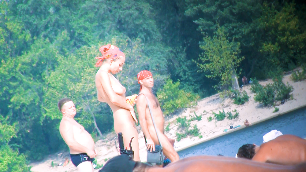 Tre nudisti riuniti su una riva boscosa di un fiume