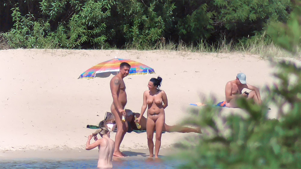 Tři nudisté pózují na písku před fotoaparátem
