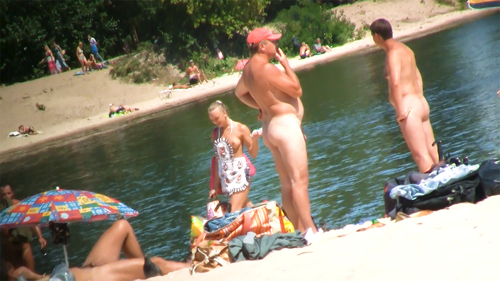 Four Naturists Chatting by the Water with Beach Bags