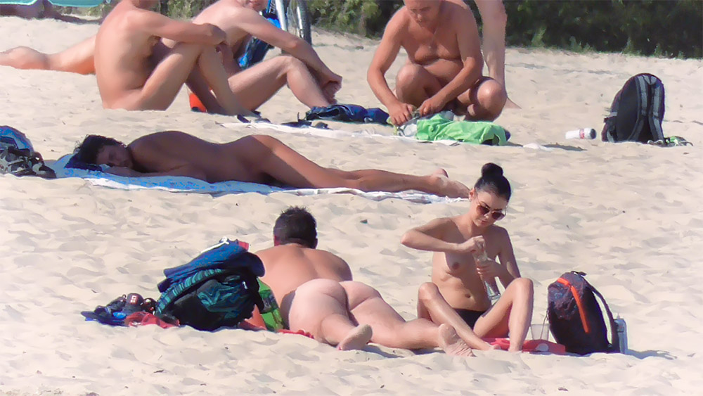 Three Beachgoers Including a Topless Woman with Sunglasses