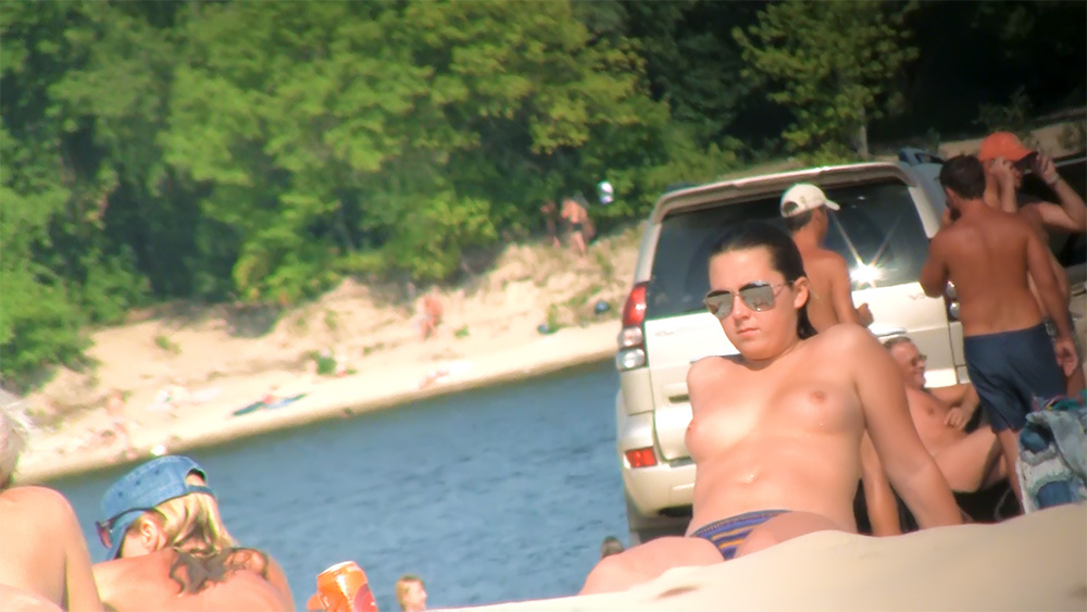 Sedící topless na rušné pláži v pilotních brýlích