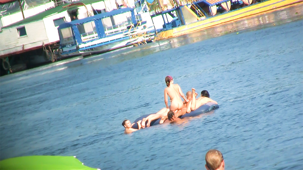 Vijf naturisten delen een drijvend luchtbed bij de oever