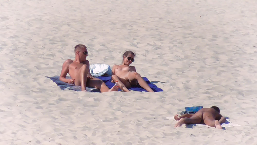 Dva nudisté opalující se spolu na písčitém pobřeží