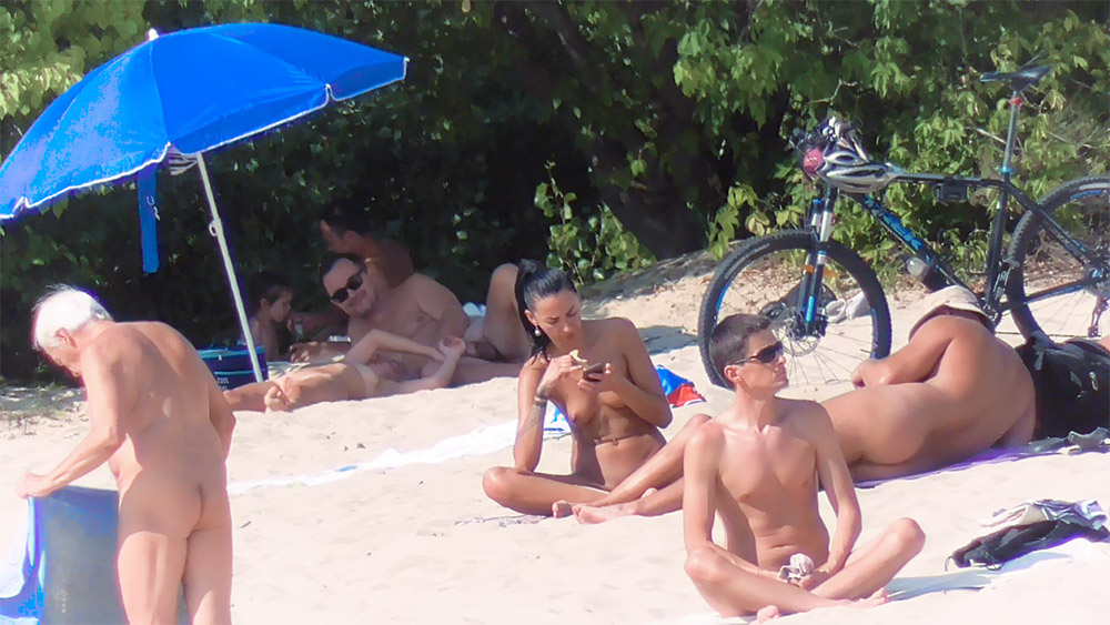 Four Naturists Resting on the Sand Near a Bicycle