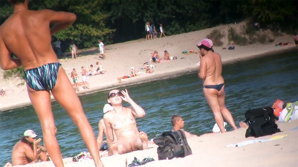 Two Nudists Resting at a Sunlit Waterfront Edge