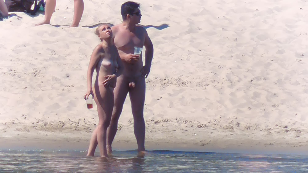 Sandy Nude Beach Shoreline with a Nudist Couple Holding Cups