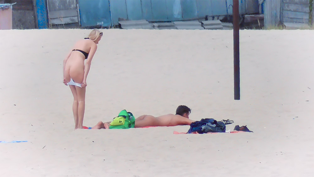 Tři nudisté na písku se zelenou taškou