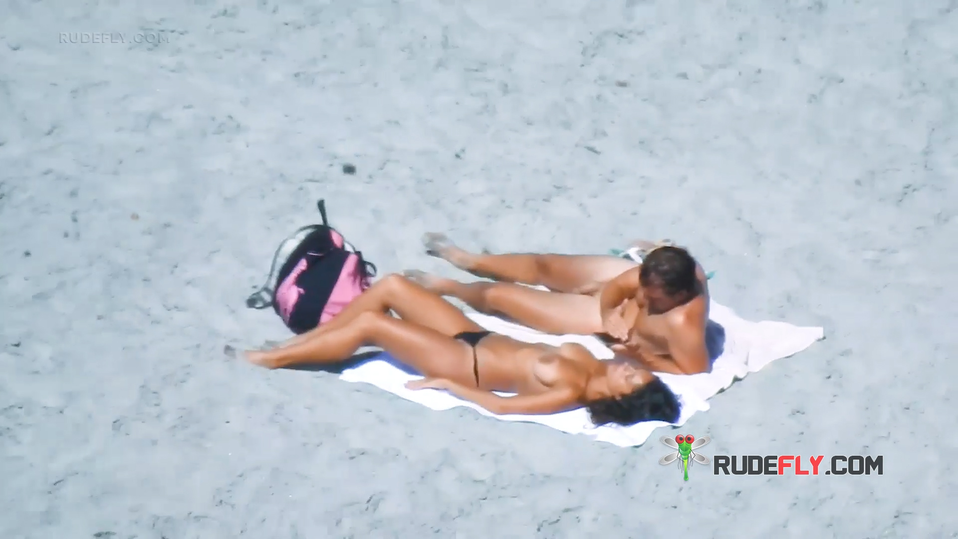 Two Topless Beach Sunbathers Beside a Pink Backpack
