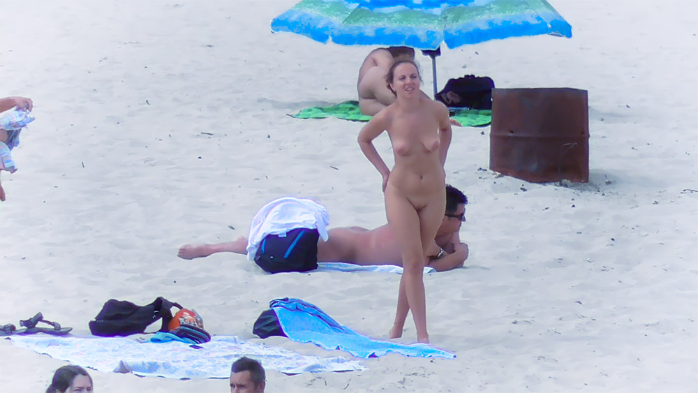 Tři naturisté odpočívající a stojící na volném písku