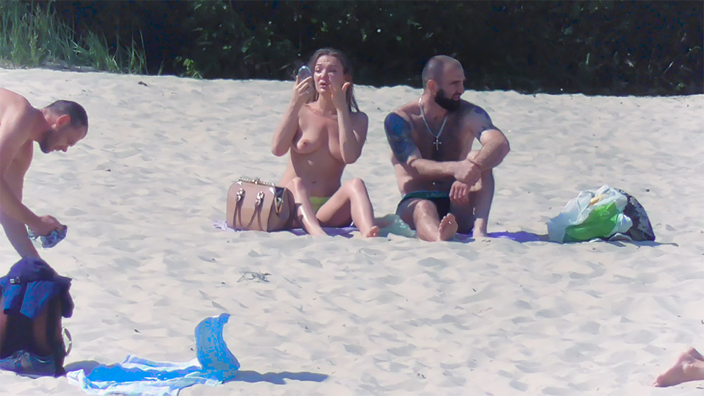 Mala castanho-clara e toalha de praia ao lado de uma banhista em topless