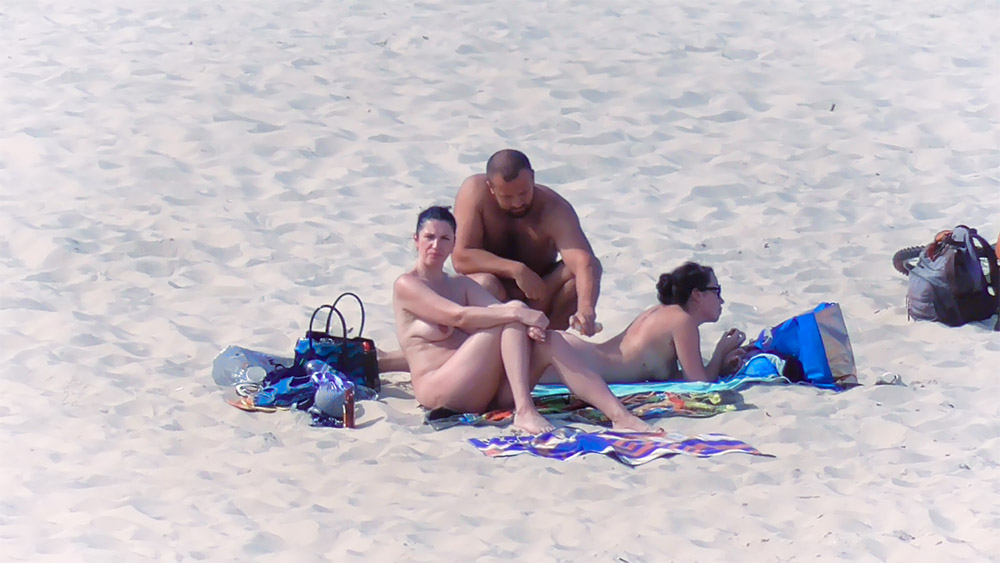 Three Nudists Resting on Patterned Towels on the Sand
