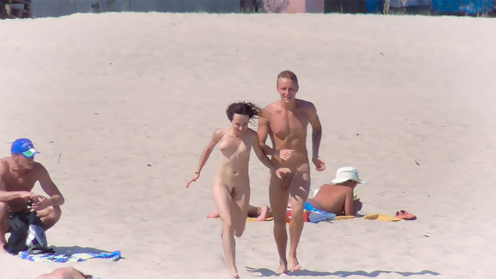 Nudistický pár běžící kolem opalujících se na písku