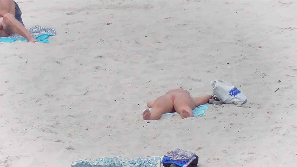 Ručník na nudistické pláži vedle plátěné tašky na světlém písku