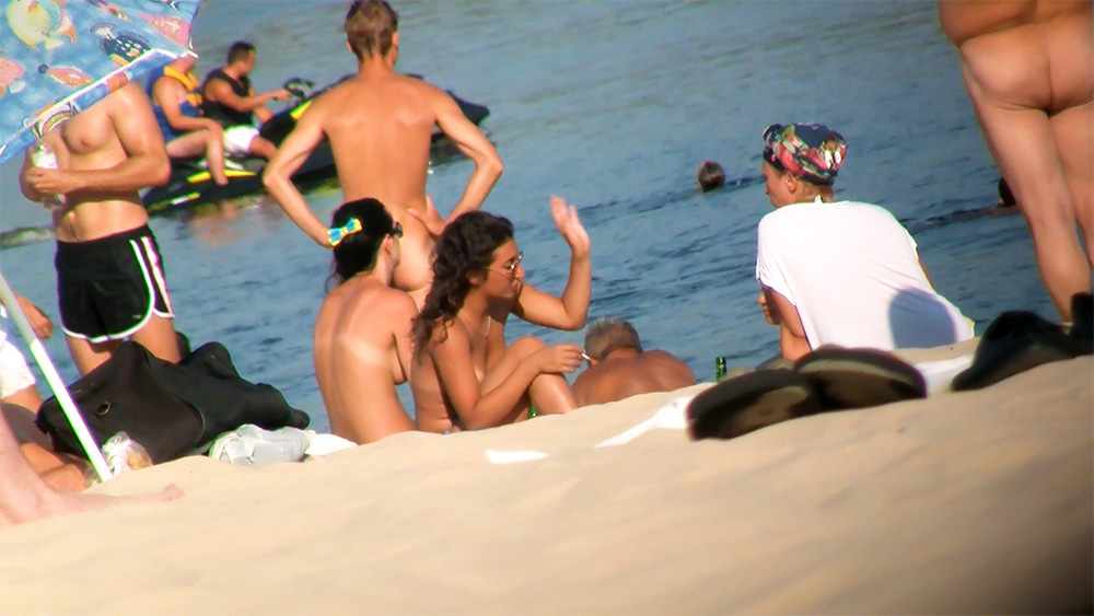Vier Nudisten auf einem Handtuch am Ufer
