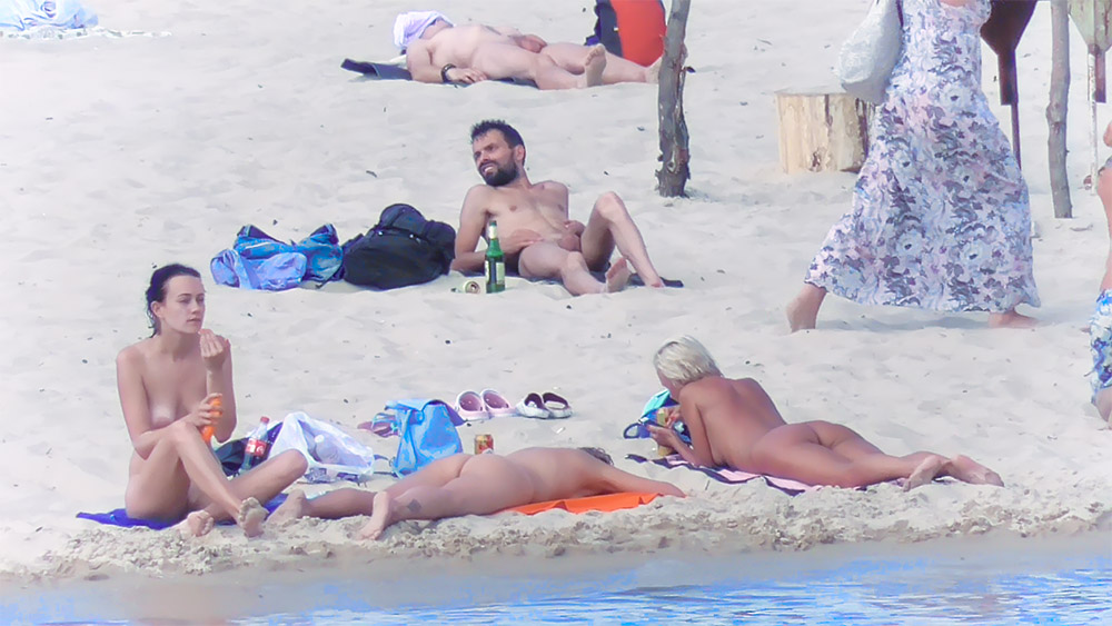 Chvíle na modré osušce na nudistické pláži s lahvičkou opalovacího krému