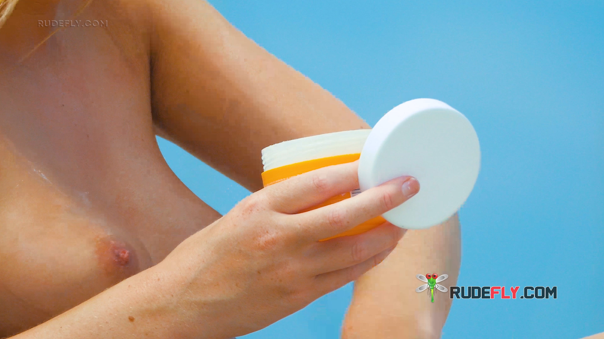 Applying Sun Cream Topless Beside Bright Blue Water