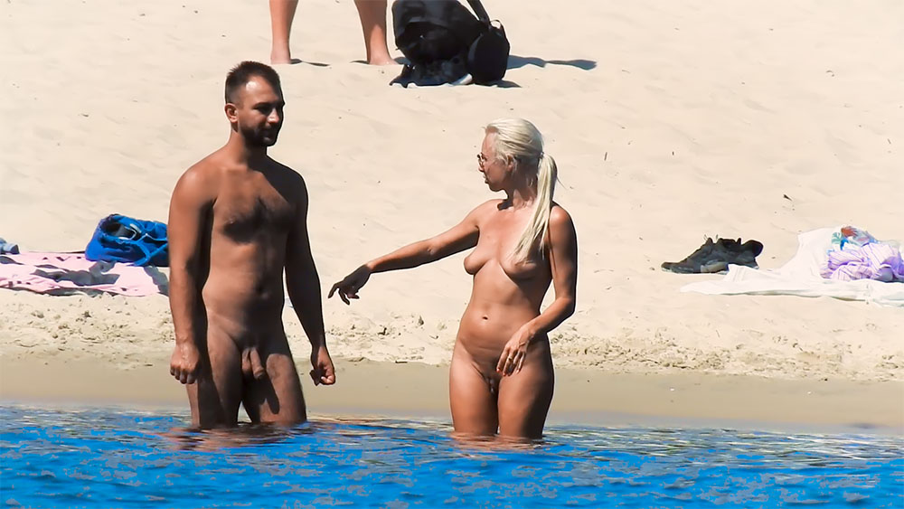 Nudist Couple Talking Together in Ankle-Deep Water