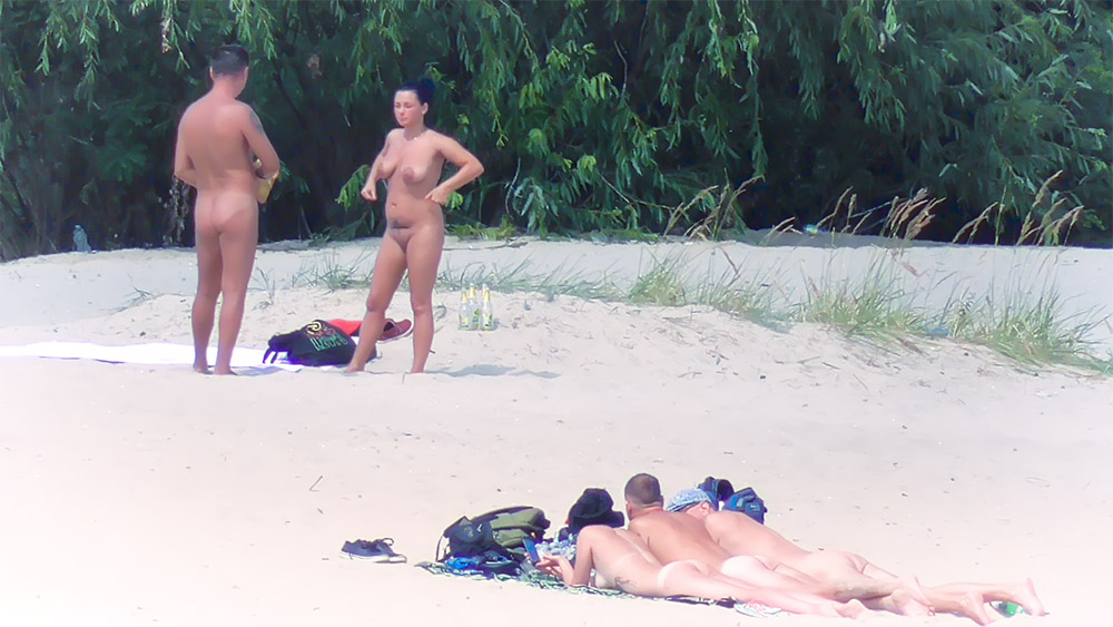 Dva nudisté povídající si u tašky na pobřeží