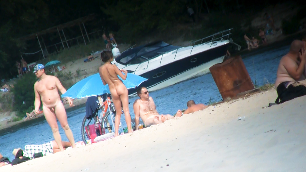 Vier nudisten verzameld bij een parasol aan het meer