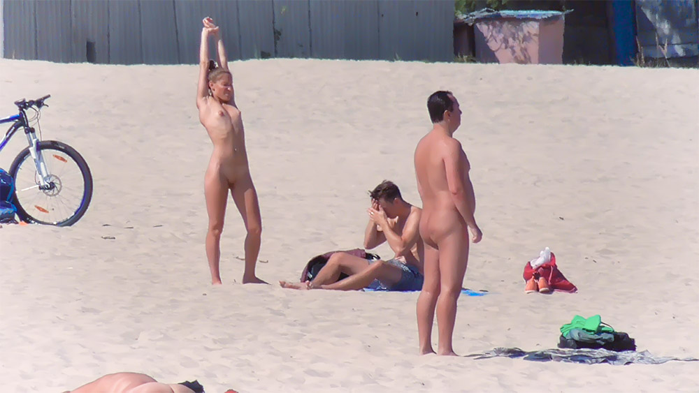 Four Nudists Gathered on Bright Beach Sand