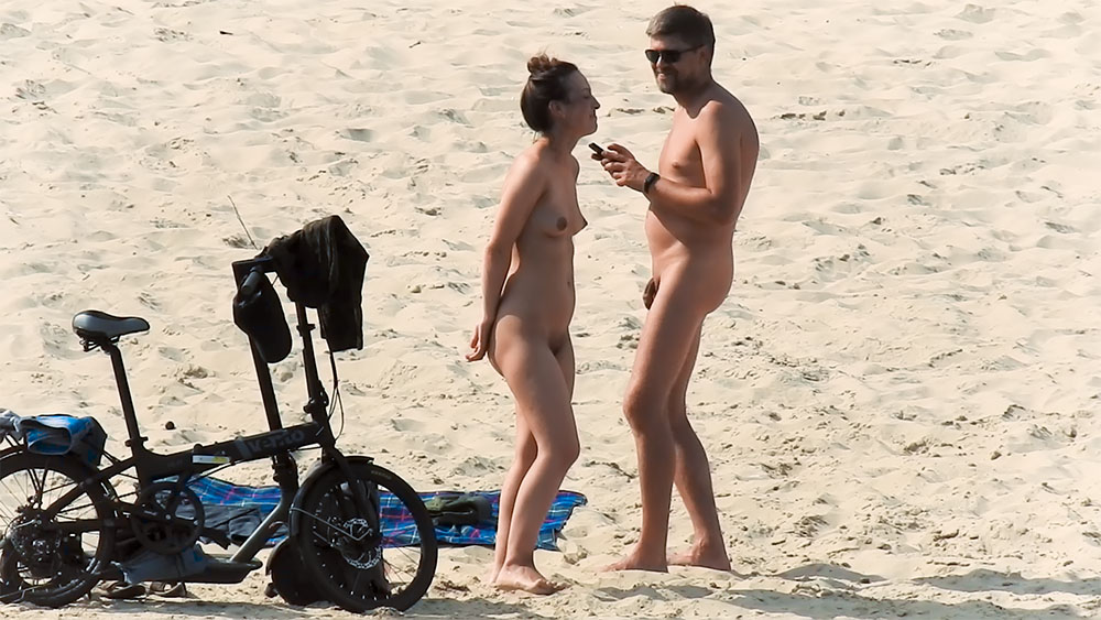 Coppia naturista in piedi che chiacchiera sulla sabbia