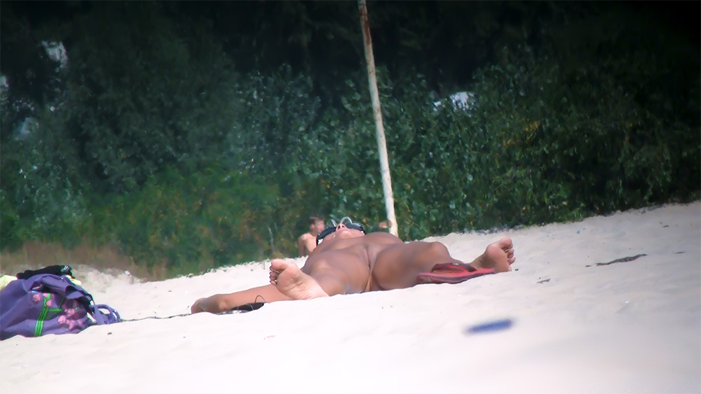 Opalující se žena na nudistické pláži s červenými žabkami na písku