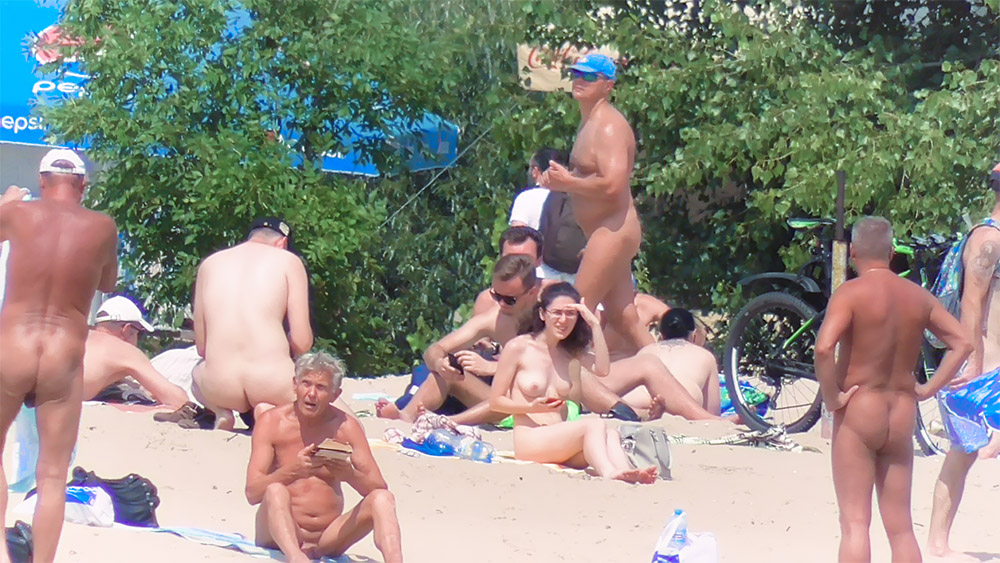 Acht naturisten zittend en staand op een zandstrand