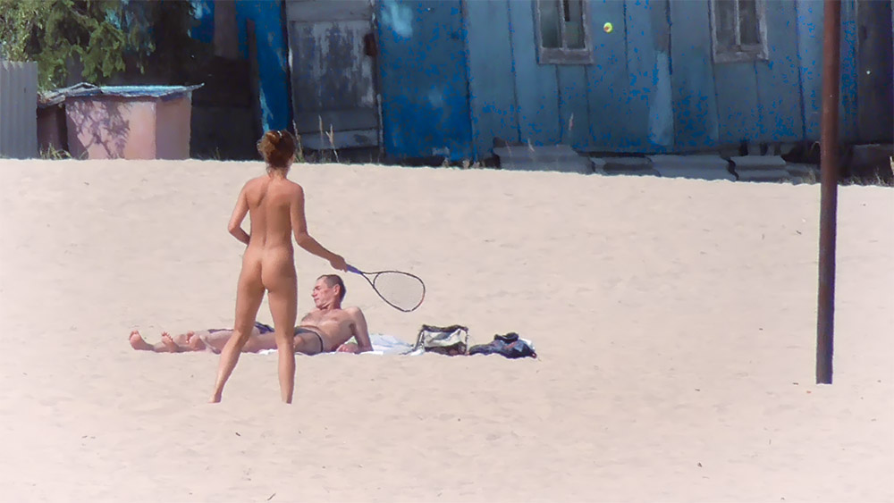Dva nudisté odpočívající s raketou na písečné pláži