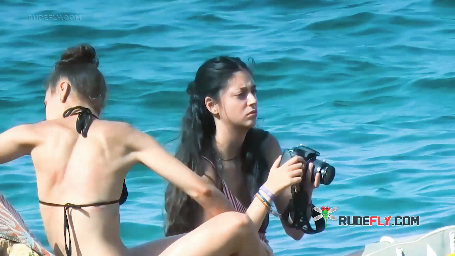 Two Topless Beach Companions Seated by the Shoreline