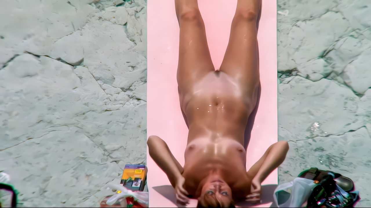 Nudist woman sunbathing on a bright pink mat over sunlit stone