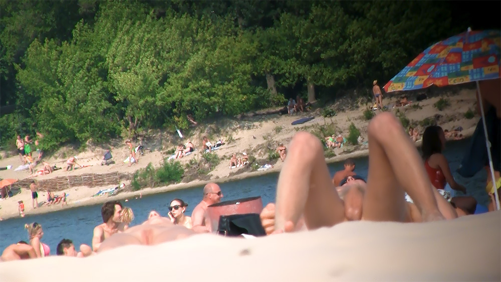 Cinque nudisti riuniti vicino all'acqua su una riva sabbiosa