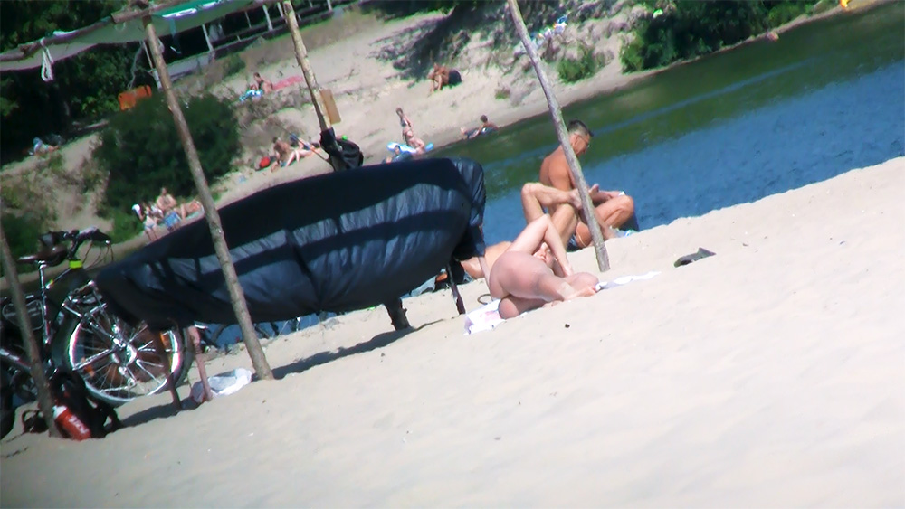 Four Nudists Resting Beside a Black Windbreak on Sand